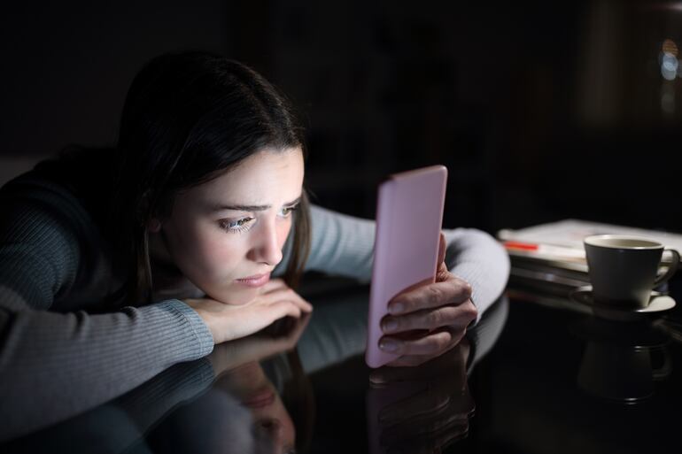 Una joven deprimida mira su teléfono celular.