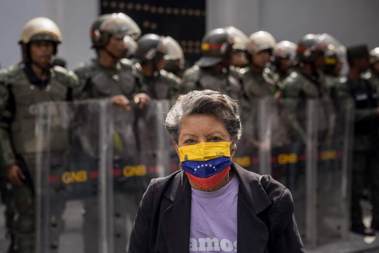 Una mujer usa una mascarilla con la bandera de Venezuela cruza frente a un pelotón de oficiales.