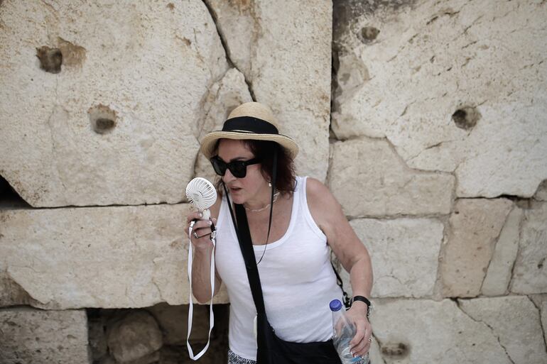 Una turista utiliza un ventilador eléctrico de mano para refrescarse en la cima de la colina de la Acrópolis durante una ola de calor, en Atenas, Grecia.  Las autoridades griegas han decidido cerrar las escuelas en algunas zonas del país y permitirán el teletrabajo a los funcionarios como medidas de prevención ante la ola de calor, con temperaturas de hasta 43 grados, que prevé entre este martes y el jueves el Servicio Meteorológico Nacional (EMI).