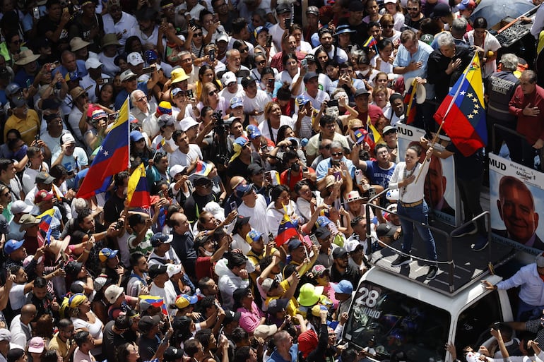 La líder de la oposición venezolana María Corina Machado (d) agita la bandera de Venezuela frente a seguidores, en Caracas.