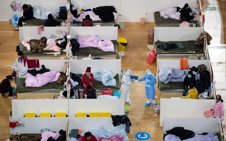 Esta fotografía tomada el 18 de febrero de 2020 muestra al personal médico caminando entre pacientes con síntomas leves del coronavirus COVID-19 que descansan por la noche en el hospital temporal instalado en un estadio deportivo en Wuhan, en la provincia central china de Hubei.