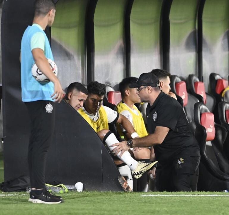 Derlis González (i), futbolista de Olimpia, es asistido por un médico en el banco de suplentes durante el partido frente a General Caballero de Juan León Mallorquín por la quinta fecha del torneo Apertura 2024 del fútbol paraguayo en el estadio Defensores del Chaco, en Asunción.