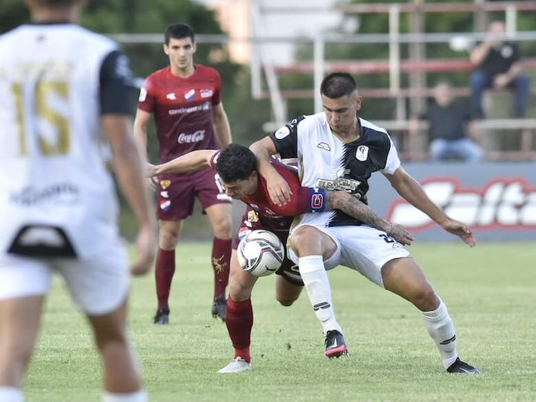 Juan Franco (rojo) de Nacional pelea por el balón con un futbolista de Tacuary en el partido de la séptima jornada del torneo Apertura 2022.