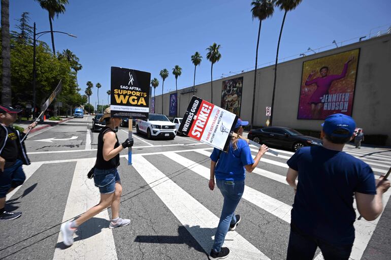 Guinistas y actores caminan con sus carteles en las afueras de los estudios Warner Bros en Burbank, California.