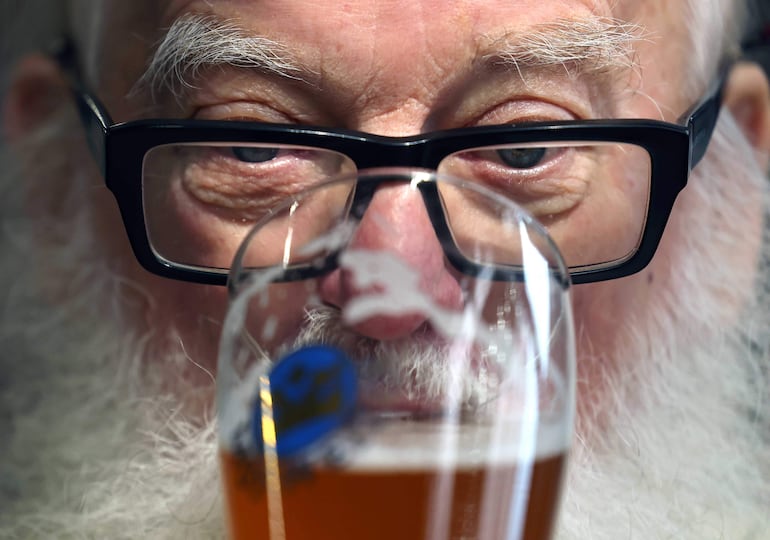 Un hombre de edad bebe un vaso de cerveza. 