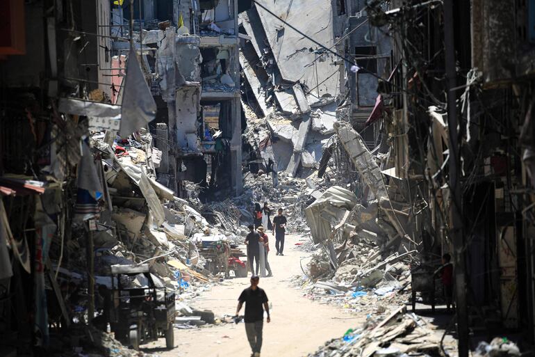 Hombres palestinos caminan por una calle estrecha pasando por edificios destruidos en Khan Yunis, en el sur de la Franja de Gaza, el 11 de junio de 2024, en medio del conflicto en curso entre Israel y el grupo militante palestino Hamás.