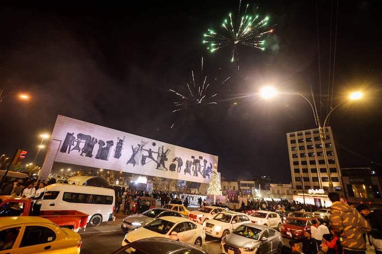 Los fuegos artificiales iluminan el cielo sobre los automovilistas en la plaza Tahrir, en el centro de Bagdad, antes de la medianoche del 31 de diciembre de 2023, antes de las celebraciones de Nochevieja. (Foto de AHMAD AL-RUBAYE / AFP)