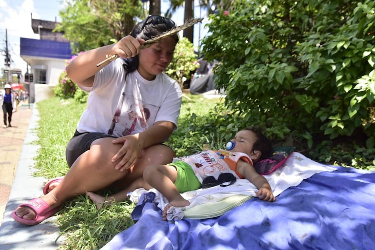 Una madre intenta proteger a su hijo del intenso calor, batiendo una pantalla de palma cerca de él.