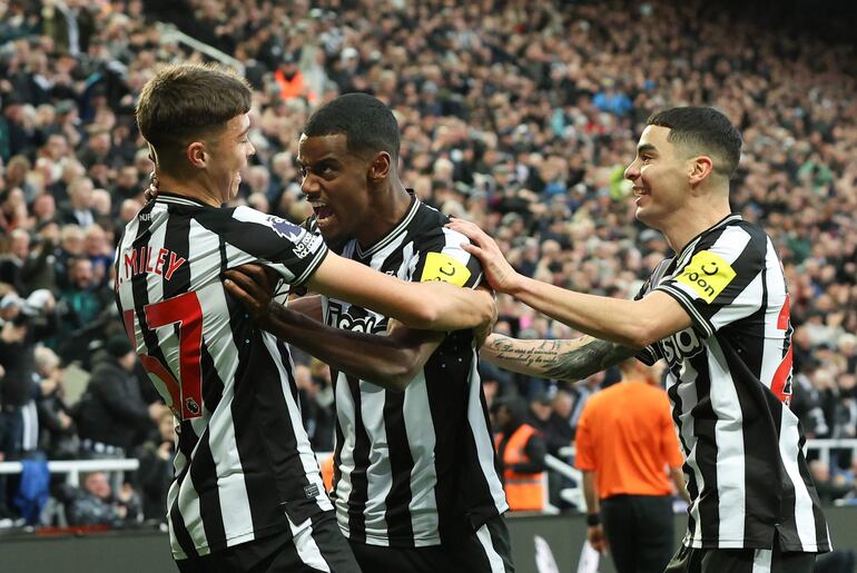 El paraguayo Miguel Almirón (d), futbolista del Newcastle, festeja un gol junto a Alexander Isak (c) y Lewis Miley (L) en un partido frente al Chelsea por la Premier League.