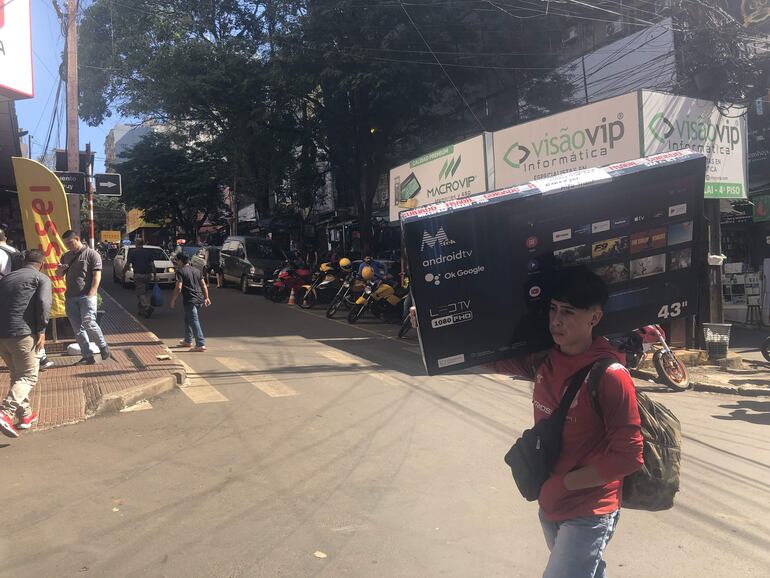 Un joven lleva una caja con televisor en una avenida del microcentro de Ciudad del Este.