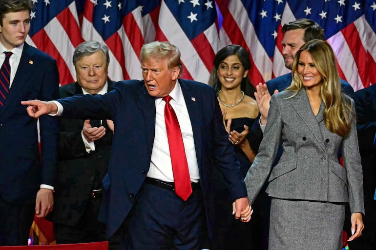 El expresidente de EE.UU. y candidato presidencial republicano Donald Trump hace un gesto a sus seguidores después de hablar mientras toma de la mano a la ex primera dama Melania Trump durante un evento de la noche electoral en el Centro de Convenciones de West Palm Beach en Florida.