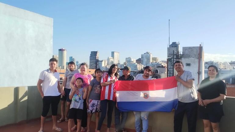 Un grupo de paraguayos residentes en Argentina posa con una bandera de Paraguay en la terraza del edificio donde viven.