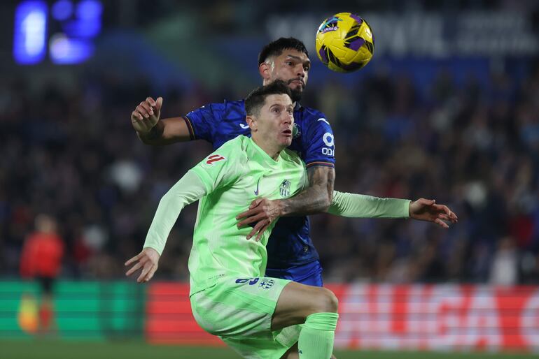 GETAFE (MADRID), 18/01/2025.- El delantero polaco del FC Barcelona, Robert Lewandowski (i), disputa el balón ante el defensa paraguayo del Getafe, Omar Alderete, durante el encuentro correspondiente a la jornada 20 de Laliga EA Sports que disputan hoy sábado Getafe y FC Barcelona en el Coliseum de Getafe. EFE / Kiko Huesca.
