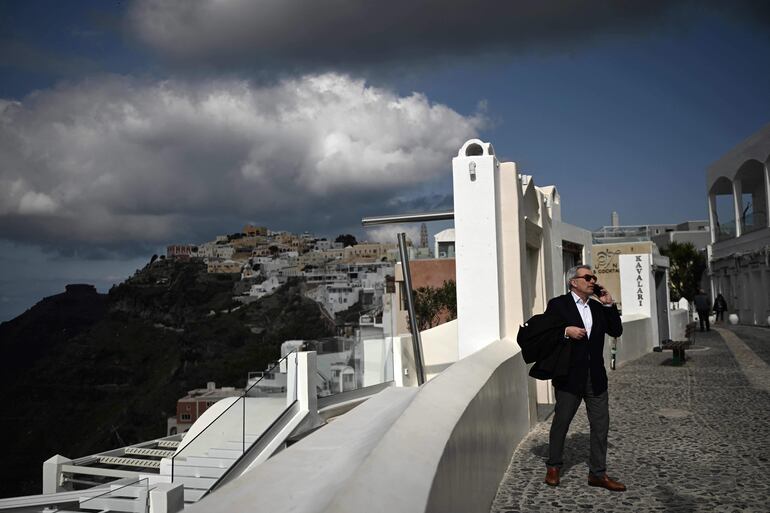 Un peatón habla por su teléfono móvil mientras camina por una calle de Fira, en la isla griega de Santorini, el 3 de febrero de 2025. Nuevos temblores durante la noche sacudieron la principal isla turística de Grecia, Santorini, según informaron los medios, lo que llevó a la gente a dormir al aire libre y a otros a irse en avión o ferry.