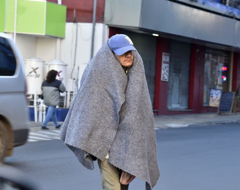 Un hombre camina con una frazada para protegerse del frío en el microcentro de Asunción.