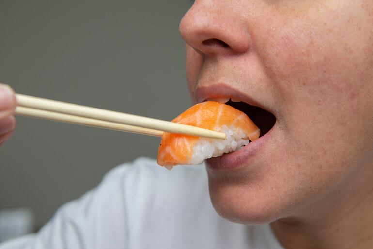 Usando palitos, una mujer se lleva a la boca un niguiri sushi de salmón.