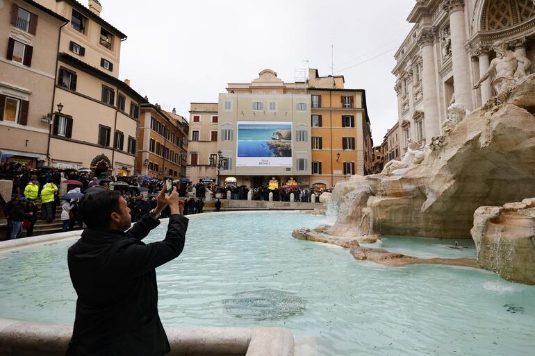 Las personas observan la Fontana de Trevi y toman fotografías mientras reabre al público tras someterse a trabajos de mantenimiento, en Roma, Italia.