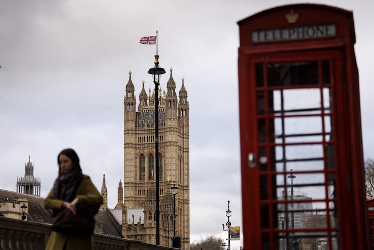 Una persona pasa por delante de unas cabinas telefónicas en Whitehall, en Londres (Reino Unido), el 06 de enero de 2025, con el Palacio de Westminster, sede del Parlamento, al fondo.