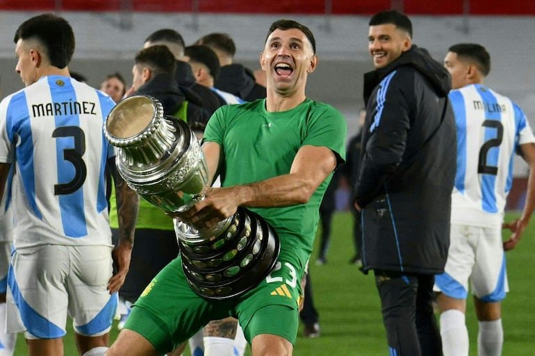 (FILES) Argentina's goalkeeper Emiliano Martinez gestures as he celebrates with a replica of the Copa America trophy after winning the 2026 FIFA World Cup South American qualifiers football match between Argentina and Chile at the Mas Monumental stadium in Buenos Aires on September 5, 2024. The Argentine Football Association (AFA) confirmed on September 28, 2024, in a statement that FIFA sanctioned goalkeeper Emiliano 'Dibu' Martinez with a two-match suspension for "offensive behavior" during the World Cup-2026 qualifiers against Chile and Colombia played in September. (Photo by Luis ROBAYO / AFP)