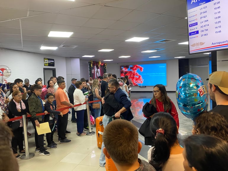 Un emotivo abrazo en la zona de arribos del aeropuerto, mientras familiares y amigos esperan con globos y regalos.