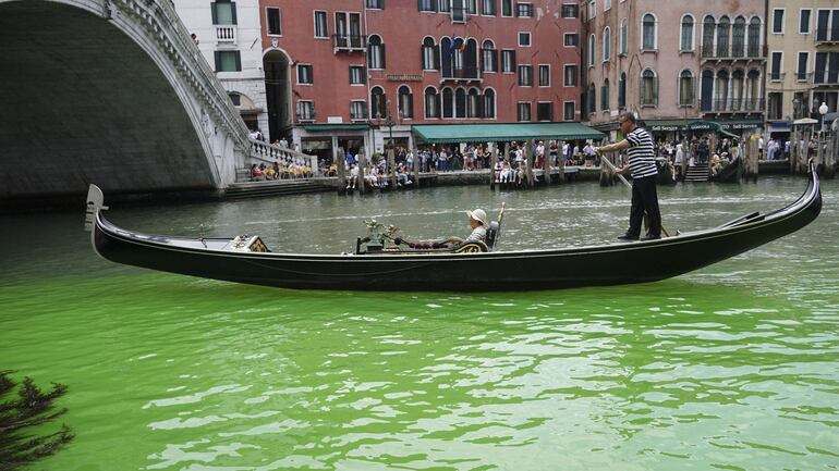 Un gondolero impulsa una góndola a lo largo de un parche de líquido verde fosforescente visto en el Gran Canal cerca del Puente de Rialto, en Venecia, Italia.